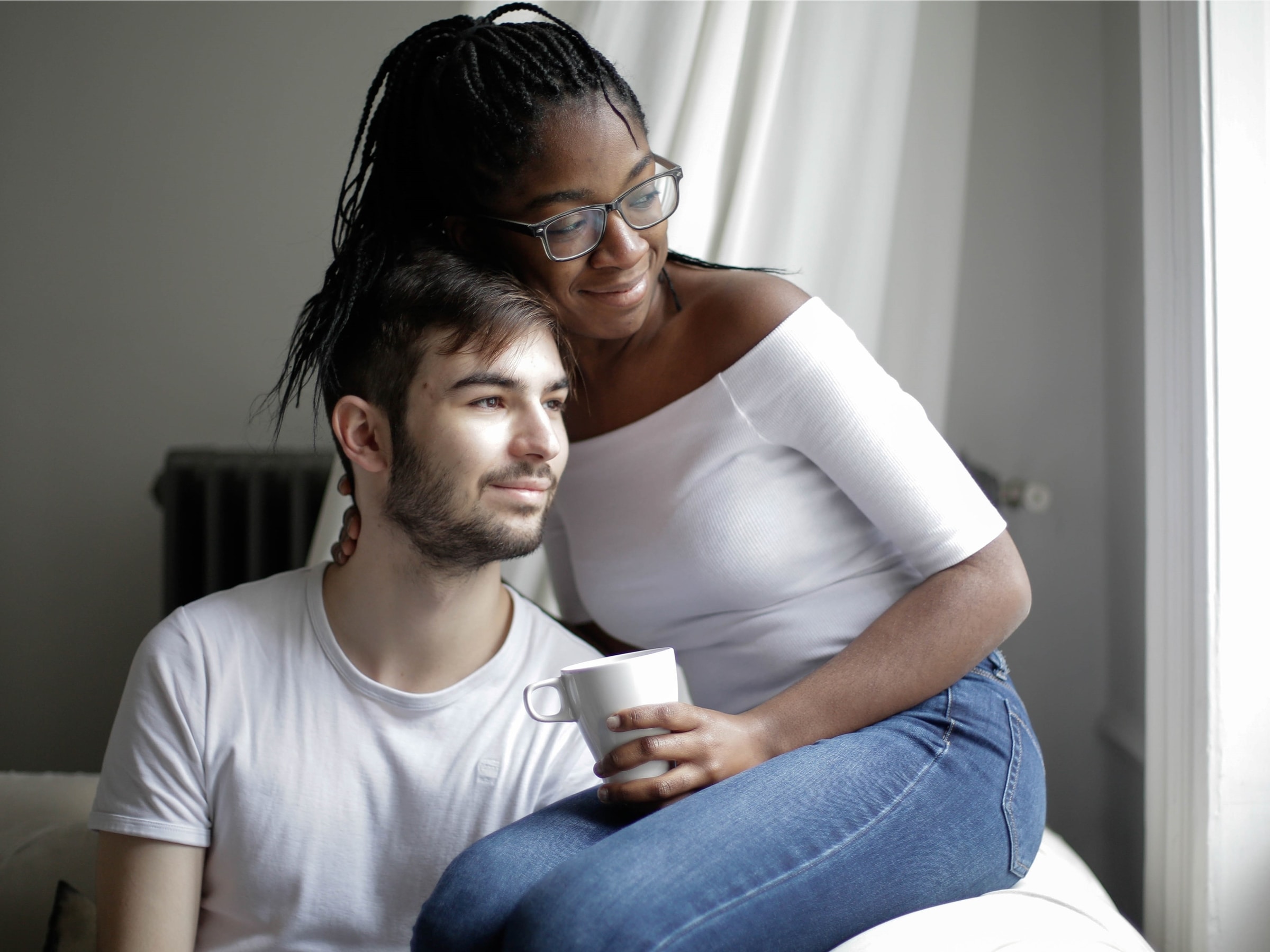 A woman holding a mug and sitting with a man as they both look out the window