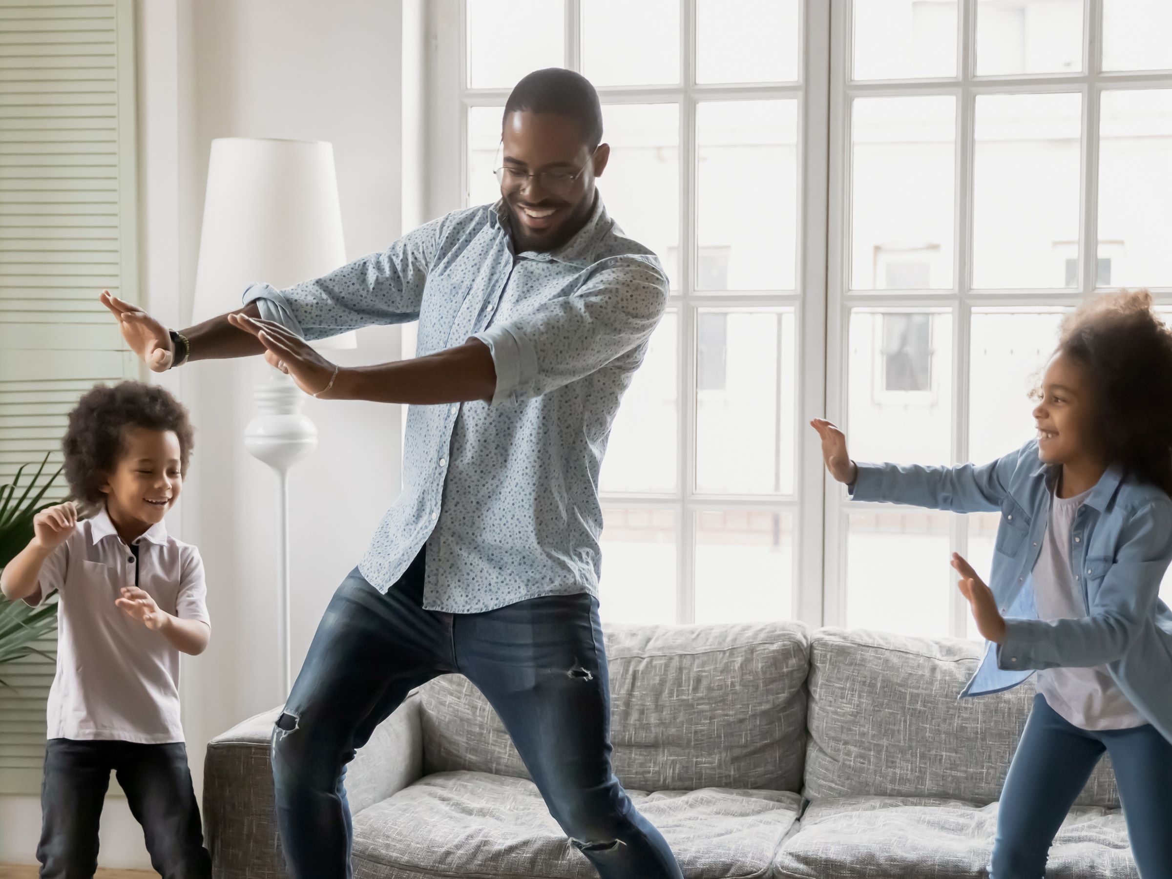 A young family is dancing infront of bright windows.