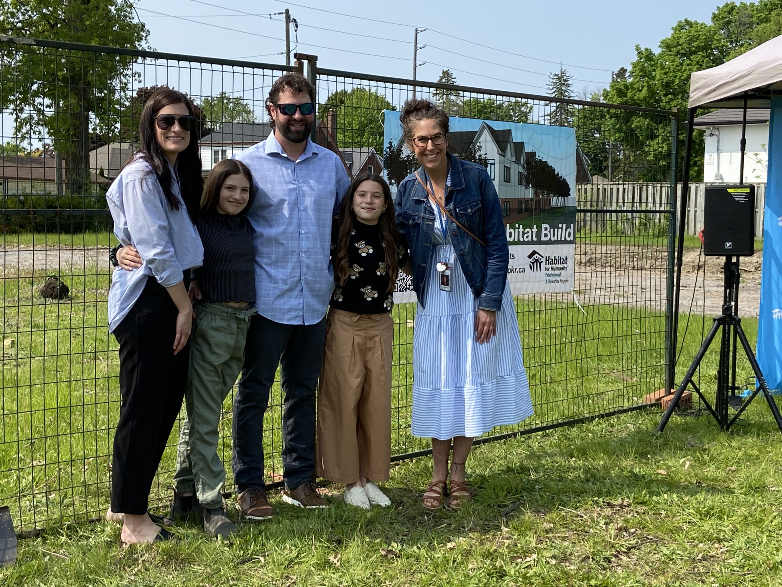 Ellyot, her family, and her teacher posing for a photo in front of the Phase 2 build site at the Build Kick-Off event on May 23