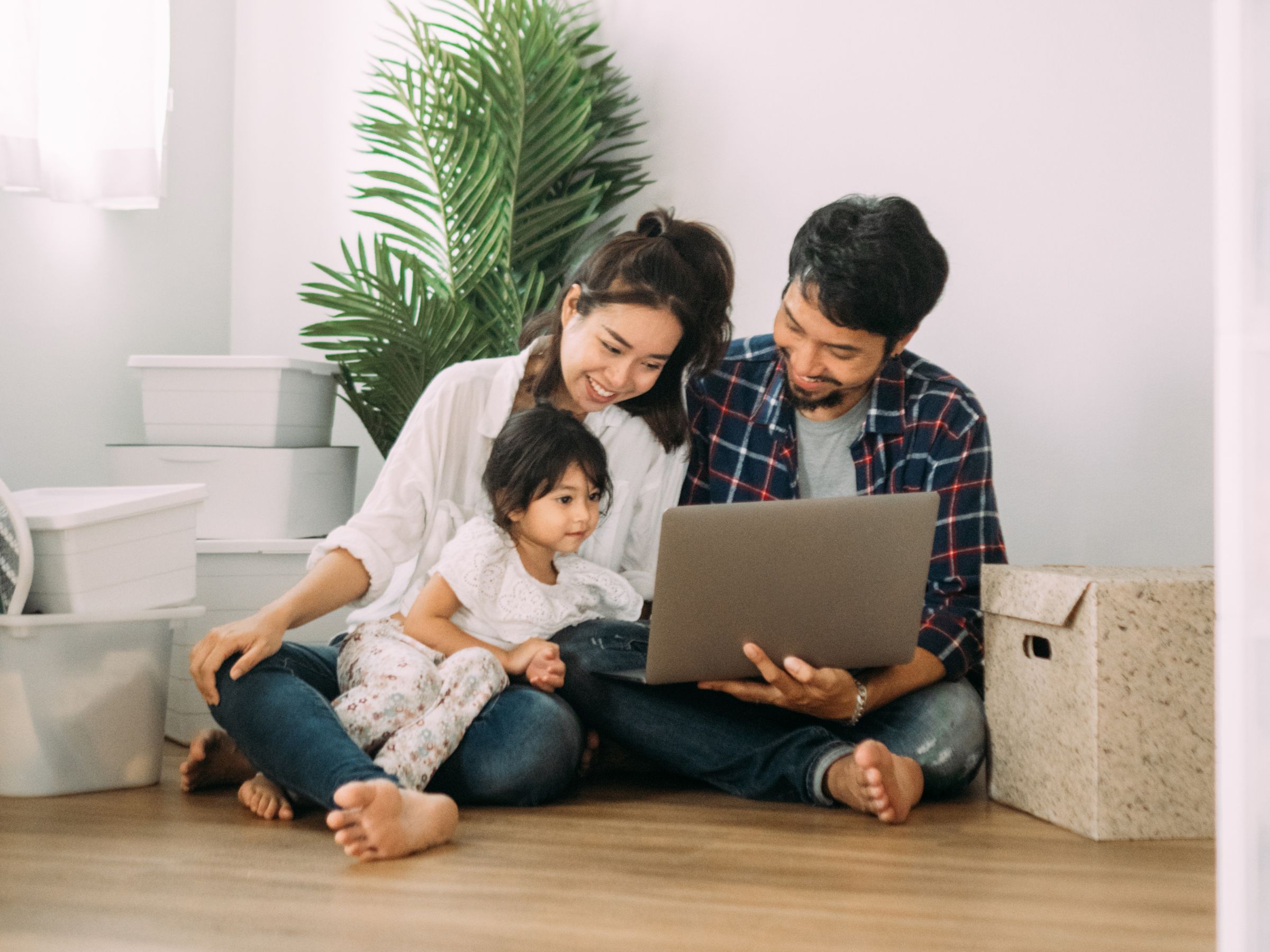 Woman, Man and Child sitting on the floor, looking at a laptop, surrounded with moving boxes in their new home