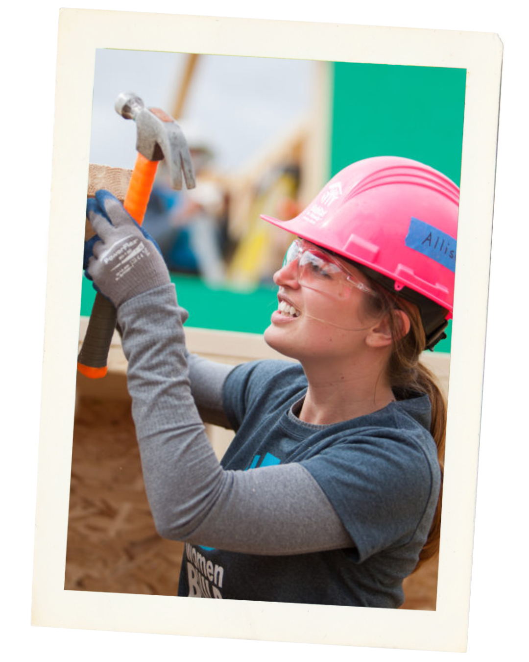 A young woman in a pink hardhat and safety glasses is holding a hammer, working on a build project.