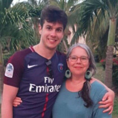 A mother and her teenage son have their arms around one another, and are smiling for the camera