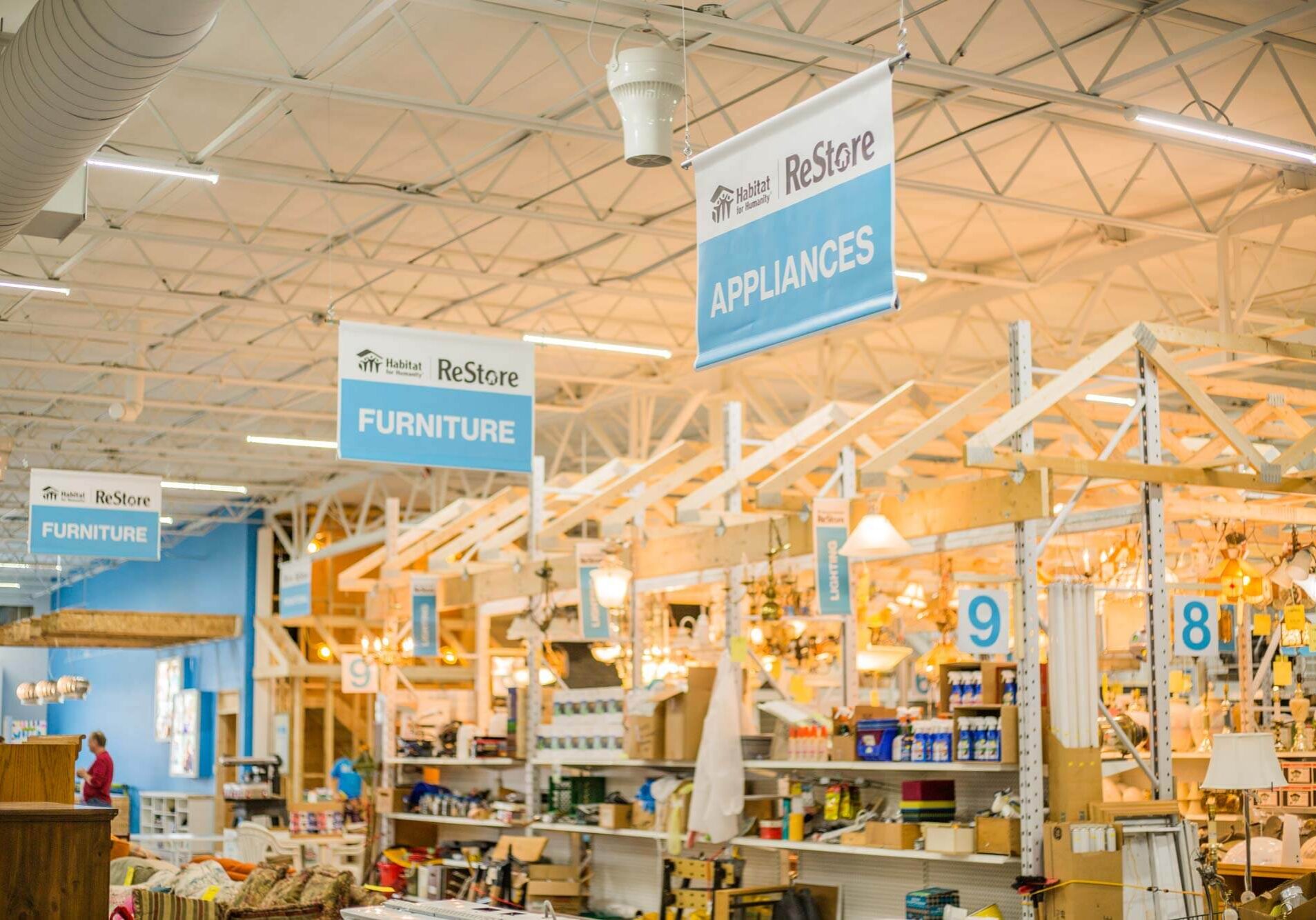 Photo of the interior of the ReStore ceiling showing the hanging aisle wayfinding banners, they read APPLIANCES, FURNITURE