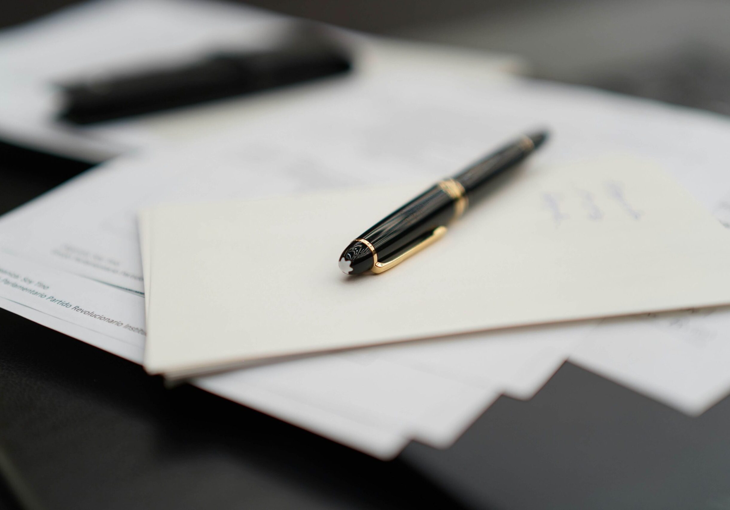 A fancy black and gold pen sits atop a pile of important looking documents